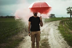 Man walking alone in the rain holding a red umbrella, representing anger management therapy